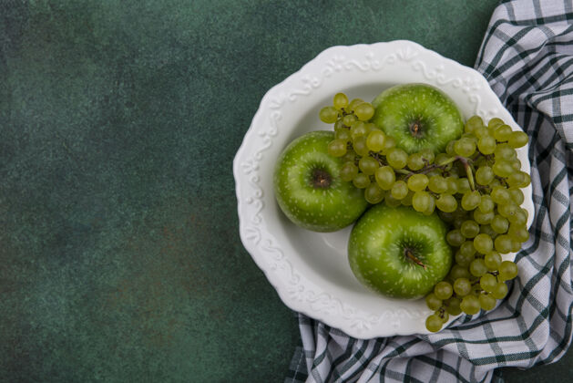 植物顶视图复制空间绿色的葡萄与绿色的苹果在一个盘子与一个格子毛巾绿色背景葡萄绿色毛巾