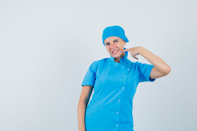 疾病女医生指着她的下巴在蓝色制服前视图站立制服肖像