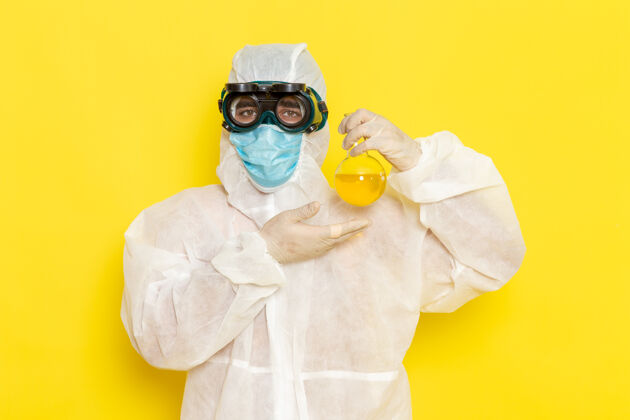化学正面图穿着特殊防护服的男科学工作者拿着黄色表面上有黄色溶液的烧瓶危险工人保护