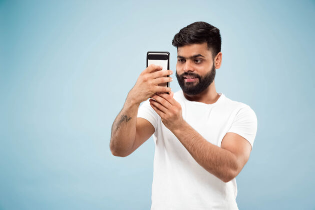 衬衫蓝色背景上穿着白衬衫的印度教年轻人的半身特写肖像人类情感 面部表情 广告概念负面空间自拍或视频博客 视频博客 聊天年轻虚拟博客专业