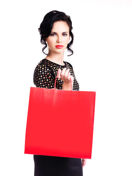 肖像一位穿着黑色连衣裙的美丽优雅的女士 白色的墙上有一个红色的购物袋女人购物者包