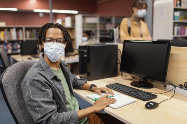 年轻戴着医学面具的男孩在图书馆学习大学Campus面罩