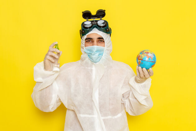 喷雾正面图男科学工作者穿着特殊的衣服拿着小圆球 喷在黄色的表面圆前面小