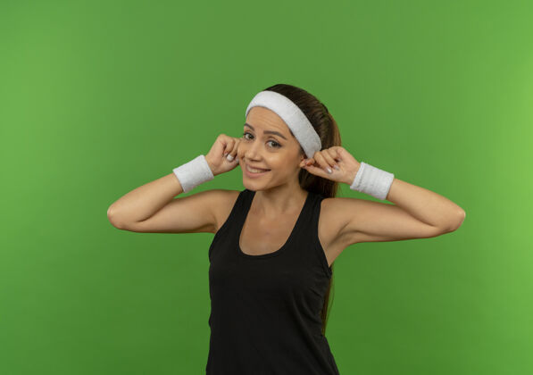 市民身穿运动服 头戴花环的年轻健身女士站在绿色的墙壁上愉快地微笑着 露出双耳运动女人运动