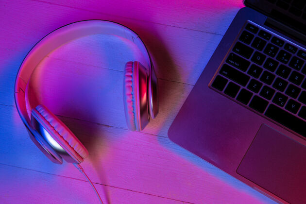 渐变紫色霓虹灯和粉色背景的一组小工具的俯视图笔记本电脑键盘 耳机和带黑屏的智能手机广告的复制空间科技 现代 小工具显示小工具空白