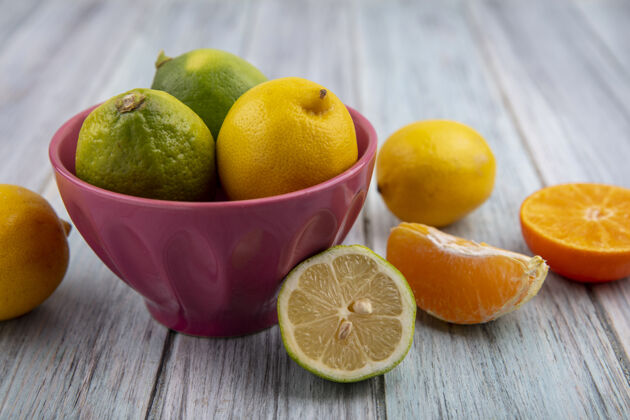 柑橘前视图柠檬与柠檬在一个碗和橙色片的灰色背景切片碗前面