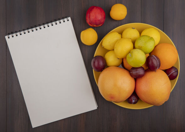 杏子顶视图复制空间柠檬与橙子李子和葡萄柚在一个黄色的碗杏子和桃子与一个记事本在木制背景顶部水果复制