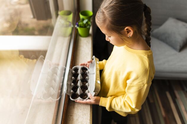 活动侧视图的小孩抱着种在鸡蛋箱里的种子在窗口栽培蔬菜种植