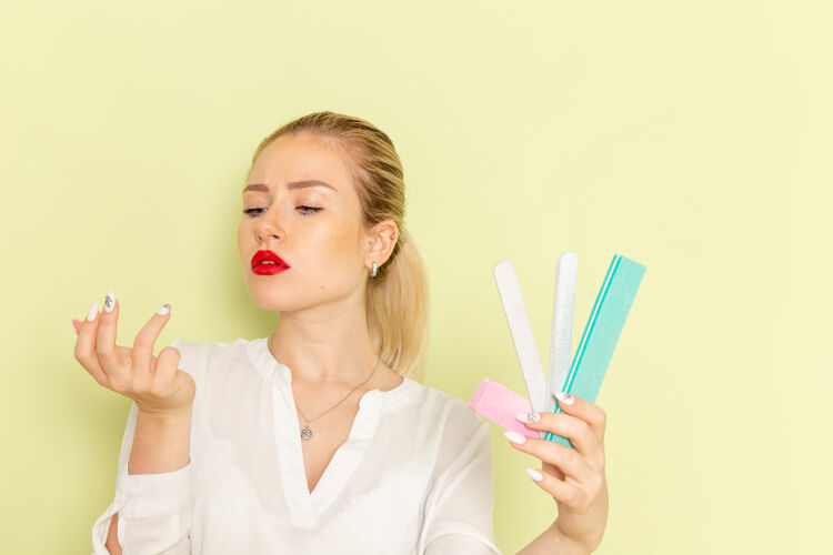 配饰正面图身着白衬衫的年轻迷人女性手持绿色表面上的美甲配件冰棍女性胡子