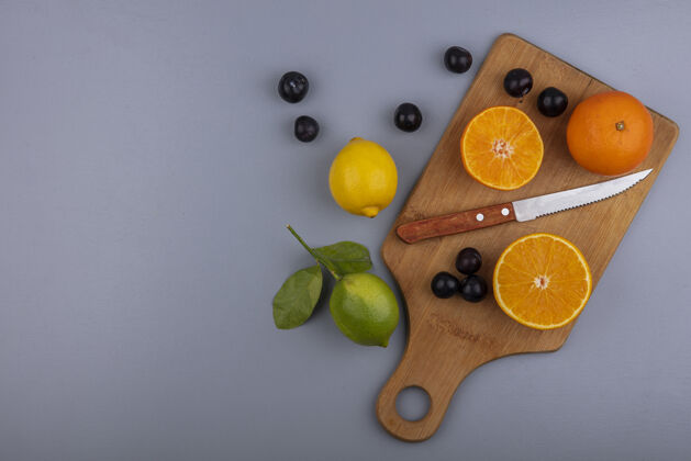柠檬顶视图复制空间用刀在砧板上的橙色切片和樱桃李子柠檬和石灰在灰色背景上顶部切片李子