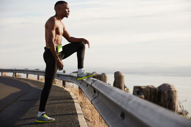 活跃决心运动的年轻人赤裸上身站在高速公路上 在路标上抬腿 早上锻炼身体 崇尚自然 喜欢运动 感到筋疲力尽 需要精力运动员慢跑视野