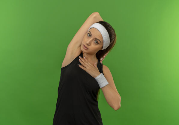 运动身穿运动服 头箍舒展的年轻健身女士站在绿色的墙上姿势她自己运动
