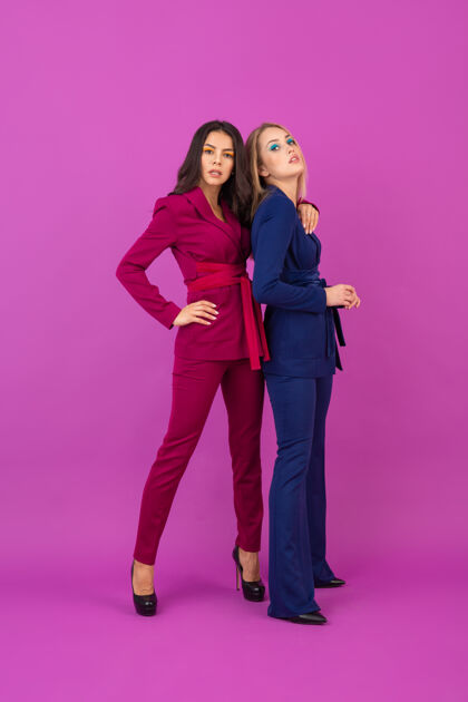 庆典高级时尚风格两位微笑迷人的女士在紫罗兰色的墙壁上穿着时尚多彩的紫色和蓝色晚礼服 朋友们一起玩 时尚潮流女士穿着优雅