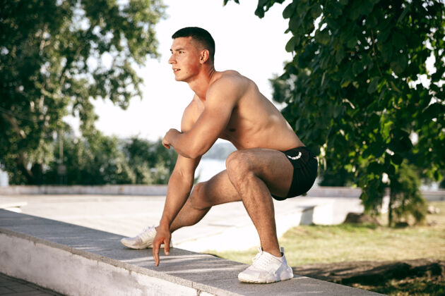 英俊一个肌肉发达的男运动员在公园里锻炼体操 训练 健身锻炼 柔韧性夏日城市在阳光明媚的日子背景场上积极健康的生活方式 青春 健美肌肉身体成人