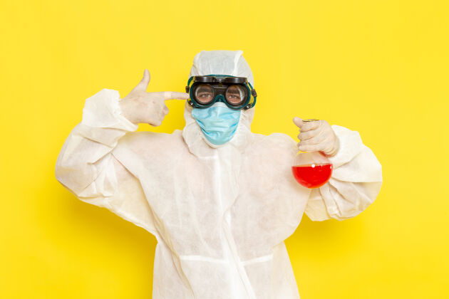 服装正面图穿着特殊防护服的男科学工作者拿着黄色表面上有红色溶液的烧瓶保护烧瓶科学