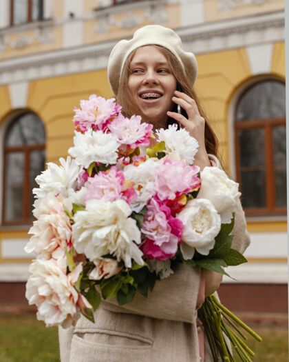 春天时髦的笑脸女人在春天捧着花束在户外打电话春天花安排