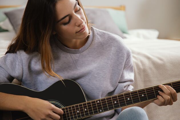 室内在家弹吉他的年轻女子的正面图女人室内娱乐