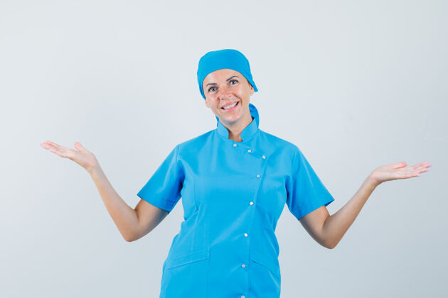疾病女医生穿着蓝色制服展示或比较某物 看上去很愉快正视图年轻人护士东西
