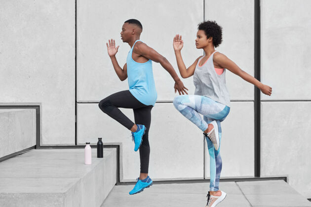 身体硬运动概念两个黑色的女性和男性助跑步骤的动作镜头 展示了良好的爬高能力 有装淡水的瓶子 以防止脱水 靠着白墙移动生活决心瓶子