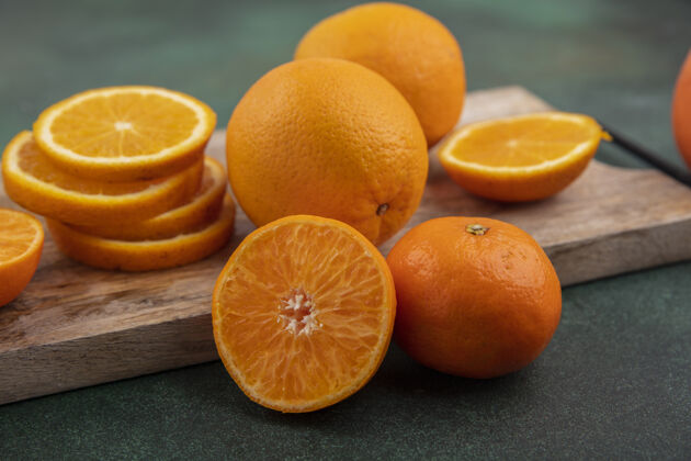 食物侧视图绿色背景上的砧板上的橙色切片板水果壁板