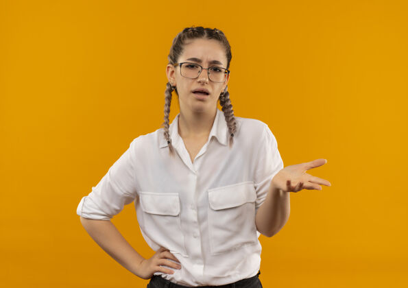 女孩一个戴着眼镜 梳着辫子 穿着白衬衫的年轻女学生站在橙色的墙上发问 看起来很不高兴 伸出手臂问手势公民