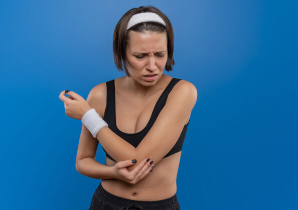 姿势穿着运动服的年轻健身女士站在蓝色的墙壁上 手肘疼痛健康触摸运动