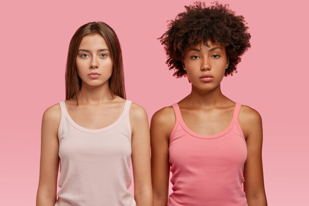 背心穿着休闲马甲的多种族女性 正经地站在粉红色的墙上 要一起进行运动训练运动最好的朋友朋友