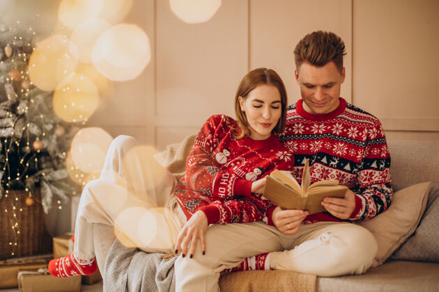 庆祝一对夫妇坐在圣诞树旁看书圣诞树甜蜜女朋友