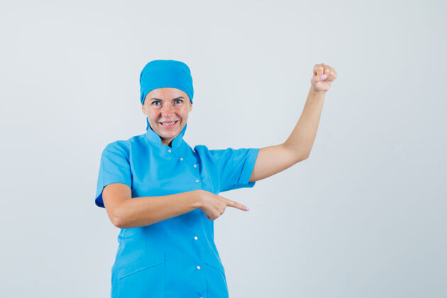 外科医生女医生指着旁边 假装拿着什么东西在蓝色制服的前视图年轻人肖像疾病