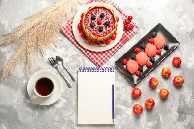 饼干俯瞰美味的奶油蛋糕与红色糖衣和饼干连同一杯茶在白色表面蛋糕饼干甜水果派饼干视图霜奶油