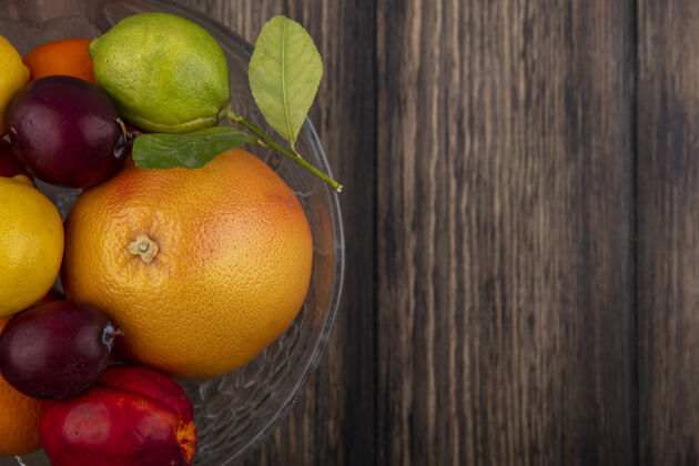 橙色顶视图复制空间水果混合柠檬 酸橙 李子 桃子和桔子在一个木制的背景花瓶复制柠檬食物