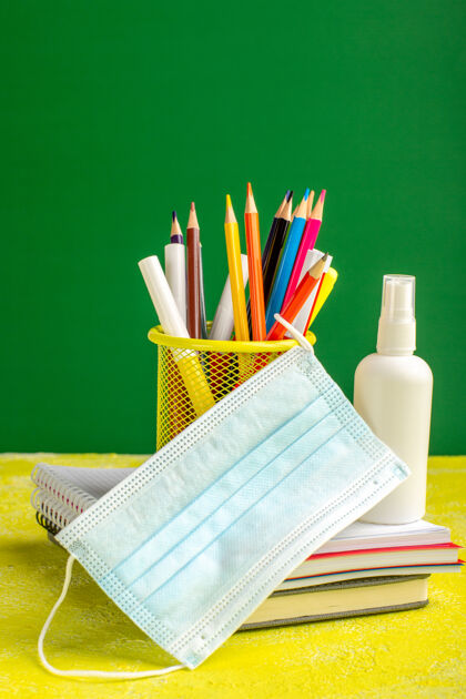 蜡笔前视图彩色铅笔与抄写本和黄色办公桌上的喷雾学校儿童喷雾