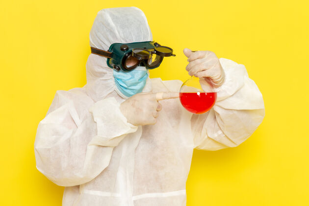套装正面图穿着特殊防护服的男科学工作者拿着黄色表面上有红色溶液的烧瓶持有配偶科学