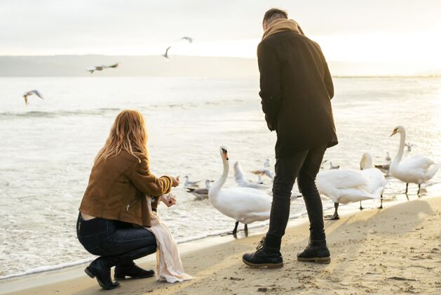 女人一对年轻的情侣在冬天的海滩上和鸟儿们在一起休闲业余爱好男人