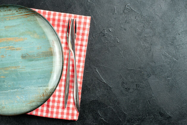 视图顶视图圆形拼盘餐刀和叉子上的红白格子餐巾上的黑色桌子自由空间玻璃圆盘子刀