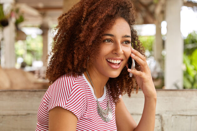 个性高兴的黑人妇女有卷曲浓密的头发的照片女性手机手机