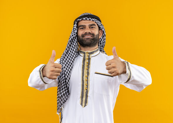 站立身着传统服装的阿拉伯商人微笑自信地站在橙色的墙上竖起大拇指传统自信微笑