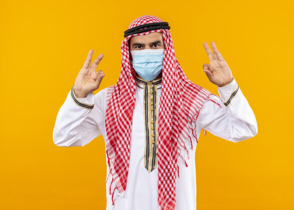 使阿拉伯商人 穿着传统服装 戴着面具 表情自信 用手指站在橙色的墙上做冥想手势冥想商务人士面具