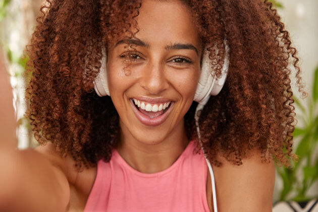 伸展快乐的黑皮肤女孩用现代立体声耳机听音乐的照片卷发手牙齿