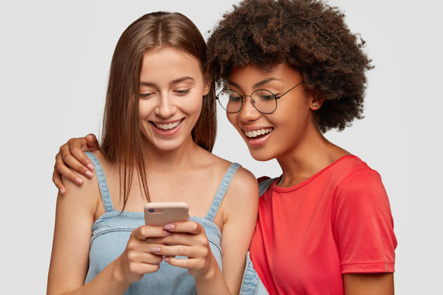 情感美丽的两个多民族姐妹通过手机在网页上一起预订的照片发型在线情感
