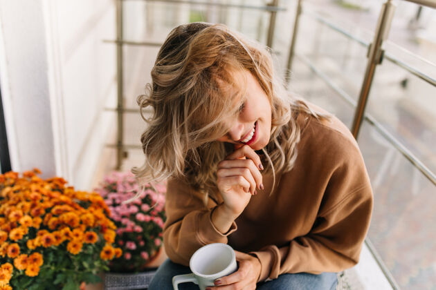 脸美丽的年轻女子在露台上喝着咖啡快乐的白人女孩微笑着坐在橙色的花朵旁模特饮料卷发
