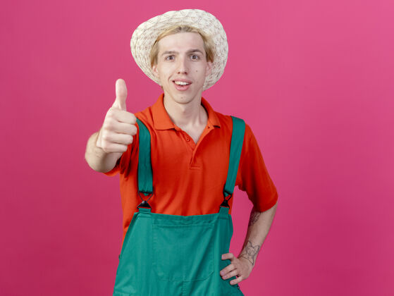 连身衣年轻的园丁穿着连体衣戴着帽子微笑着竖起大拇指微笑穿年轻人