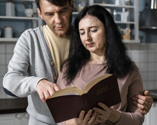 信条男人和女人在厨房阅读圣经的正面图祈祷宗教崇拜