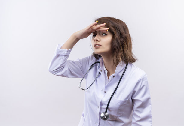 年轻人穿着白大褂的年轻女医生拿着听诊器遥望远方 机智地把头伸过来看某人或某事外套医生某人