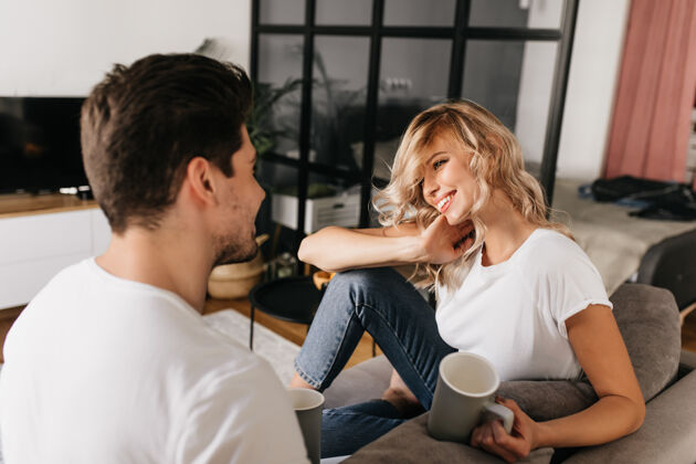 男人一位金发碧眼 满脸笑容的漂亮年轻女子看着她的男朋友幸福的一对坐在家里的沙发上关系乐趣卧室