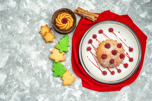 顶部俯视图白色椭圆形盘子上的浆果蛋糕红色披肩肉桂棒饼干在灰色表面早餐盘子胡椒