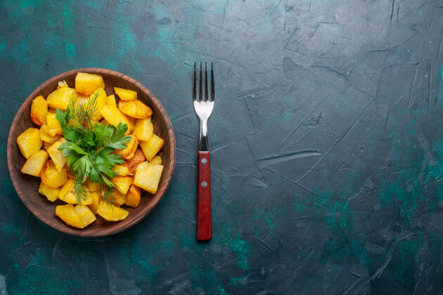 土豆俯视图深蓝色桌子上棕色盘子里放着烤土豆片和绿色蔬菜的美味一餐食物里面深蓝色