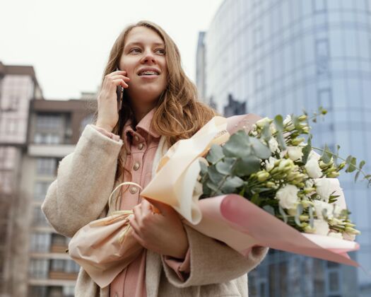 春天优雅的女人在户外用智能手机聊天 手里拿着一束鲜花户外花安排