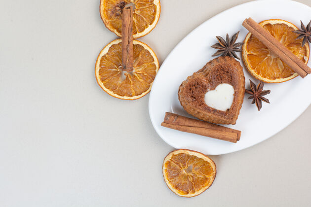 形状心形奶油蛋糕 橘子片 丁香和肉桂放在白色盘子里甜面包房蛋糕