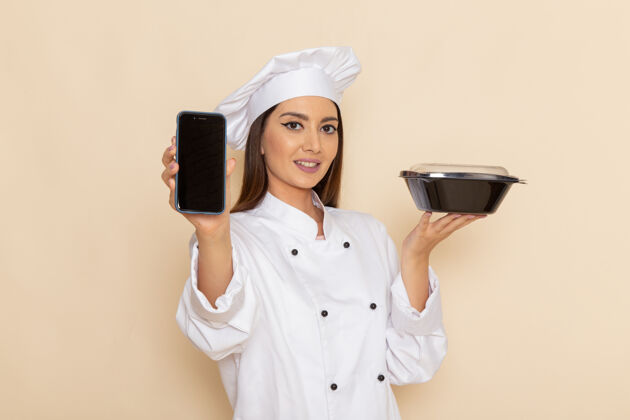 碗身穿白色厨师服的年轻女厨师正对着白色墙上拿着电话和黑碗女性烹饪工人